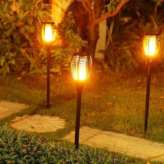 Antorcha solar con efecto de llama encendida entre plantas de noche