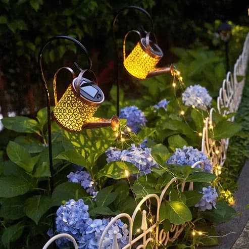 Regadera solar con cascada de luces sobre un cantero de flores de noche